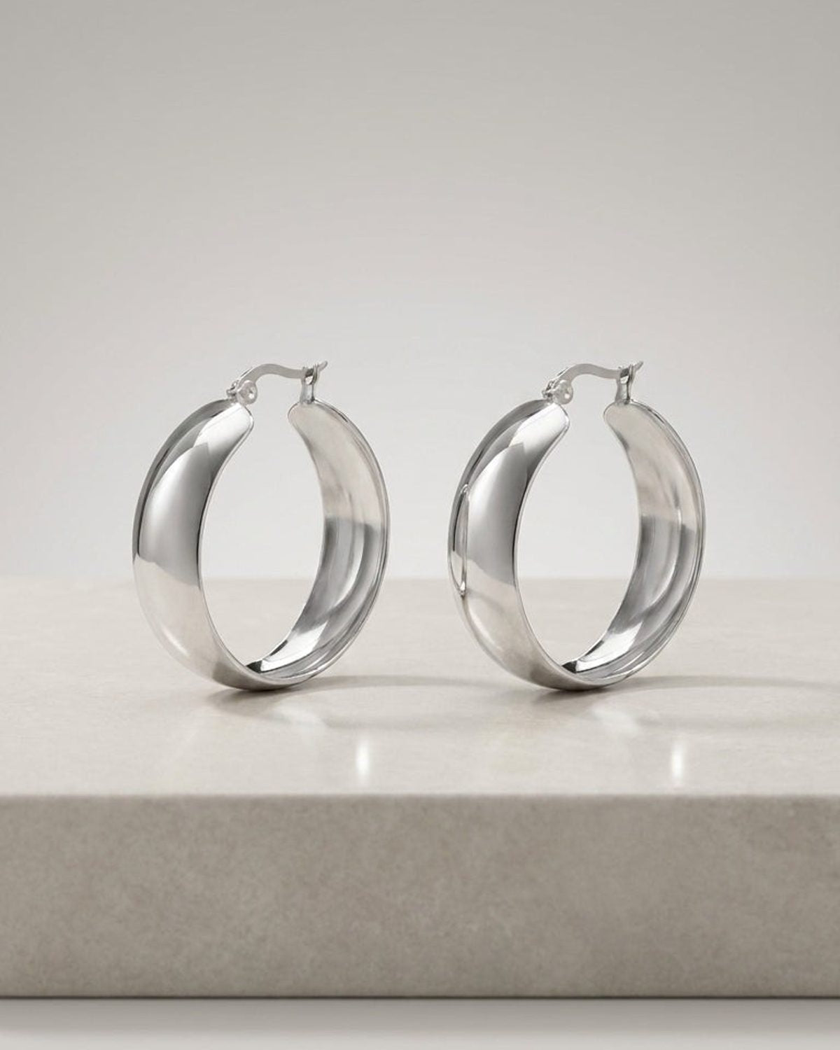 Polished silver thick hoop earrings by House of Lily, featuring a smooth, chunky modern design on a neutral surface.