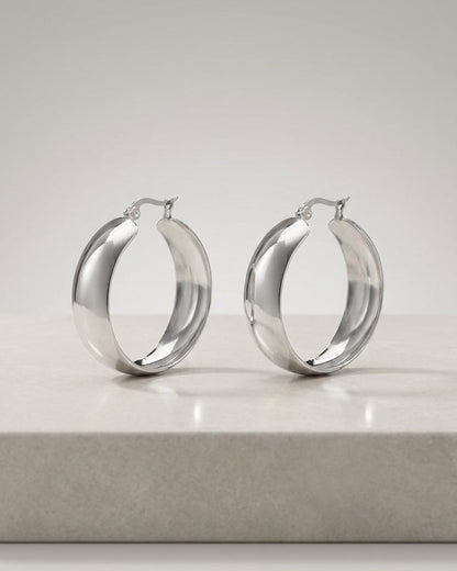 Polished silver thick hoop earrings by House of Lily, featuring a smooth, chunky modern design on a neutral surface.
