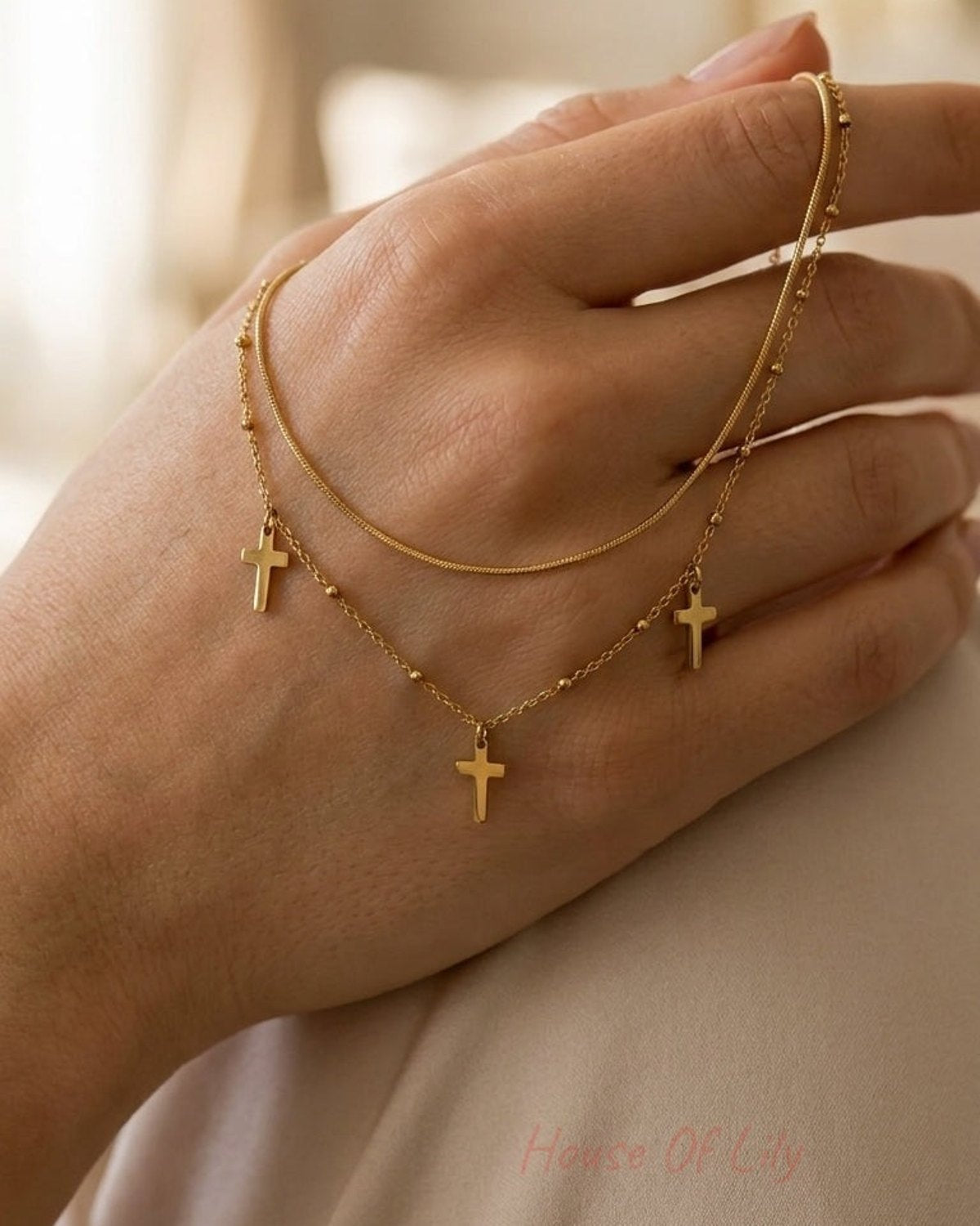 Double-strand gold necklace held in hand, featuring three small cross charms and delicate bead accents.