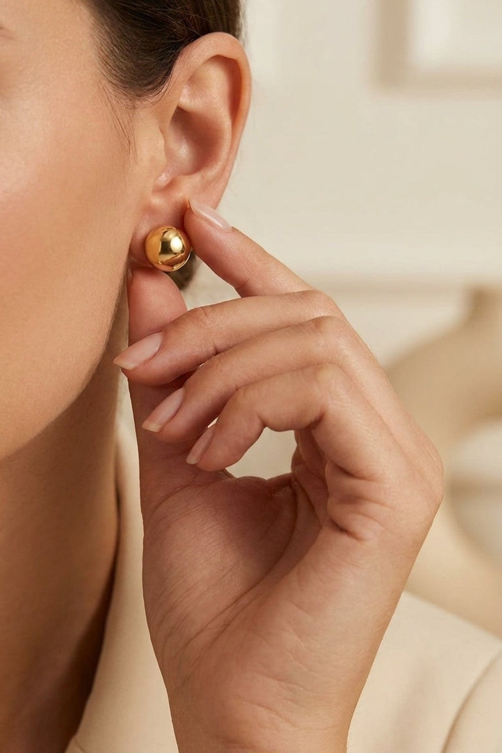 Chic Steel Geometric Studs: polished gold spherical stud earrings worn on an earlobe.