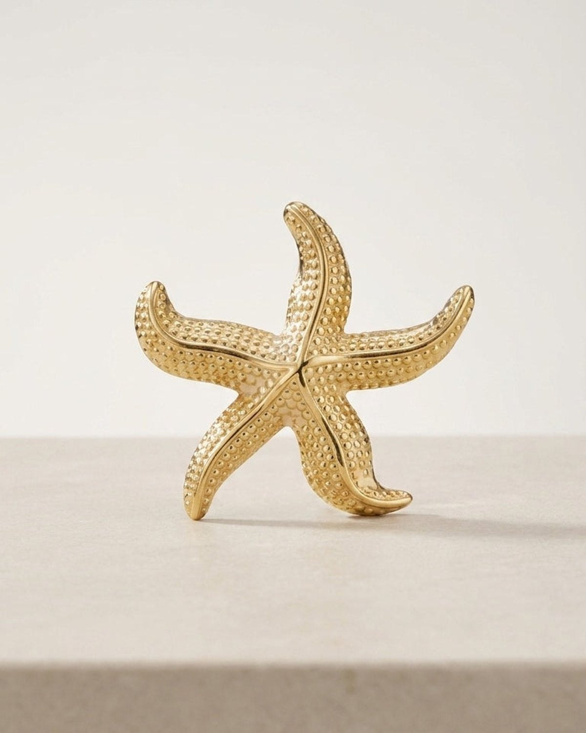 Gold starfish pin with a textured, dotted surface displayed upright on a light surface.