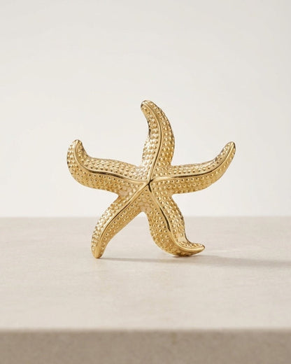 Gold starfish pin with a textured, dotted surface displayed upright on a light surface.