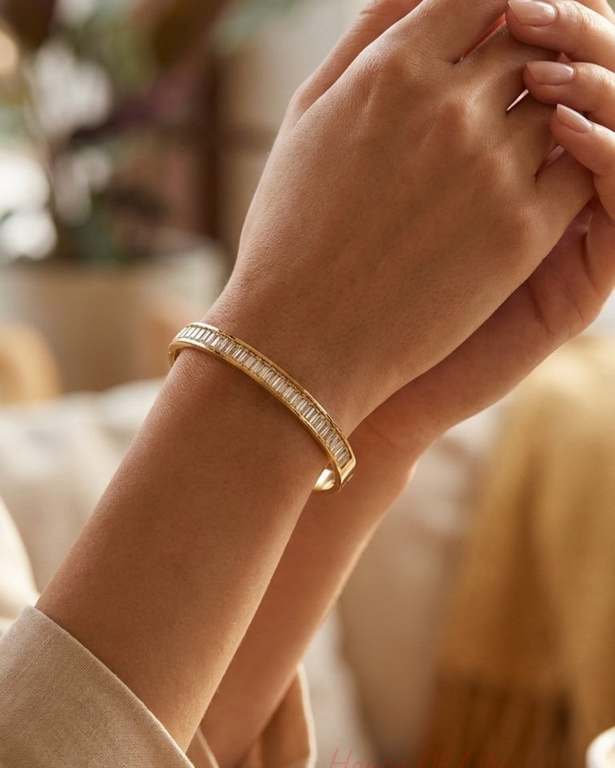 A gold cuff bracelet, channel-set with rectangular baguette crystals, worn on a woman’s wrist.