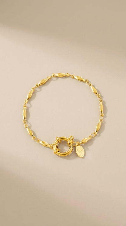 Gold oval chain bracelet with a large round clasp and small logo charm.