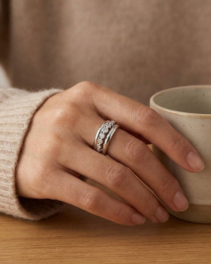A silver ring with embedded rhinestones is worn on a hand holding a ceramic mug.