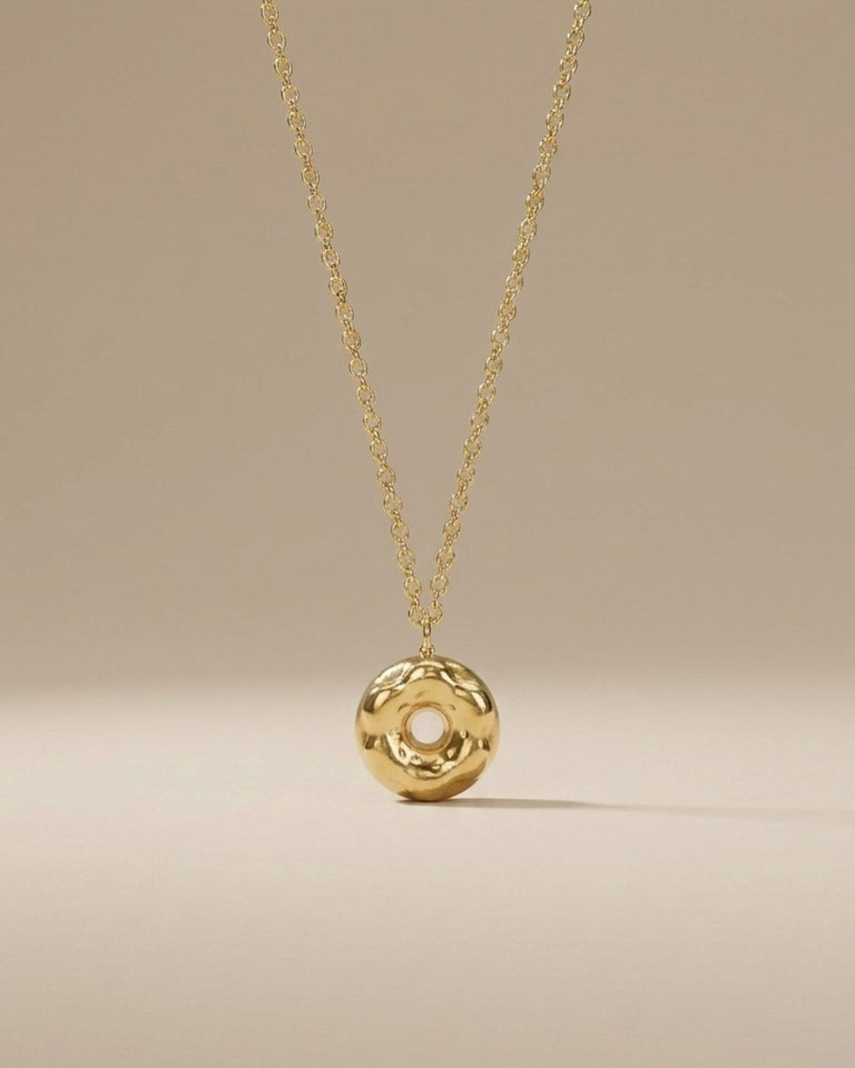A shiny gold donut-shaped pendant hangs from a matching chain against a neutral background.