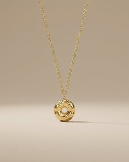 A shiny gold donut-shaped pendant hangs from a matching chain against a neutral background.