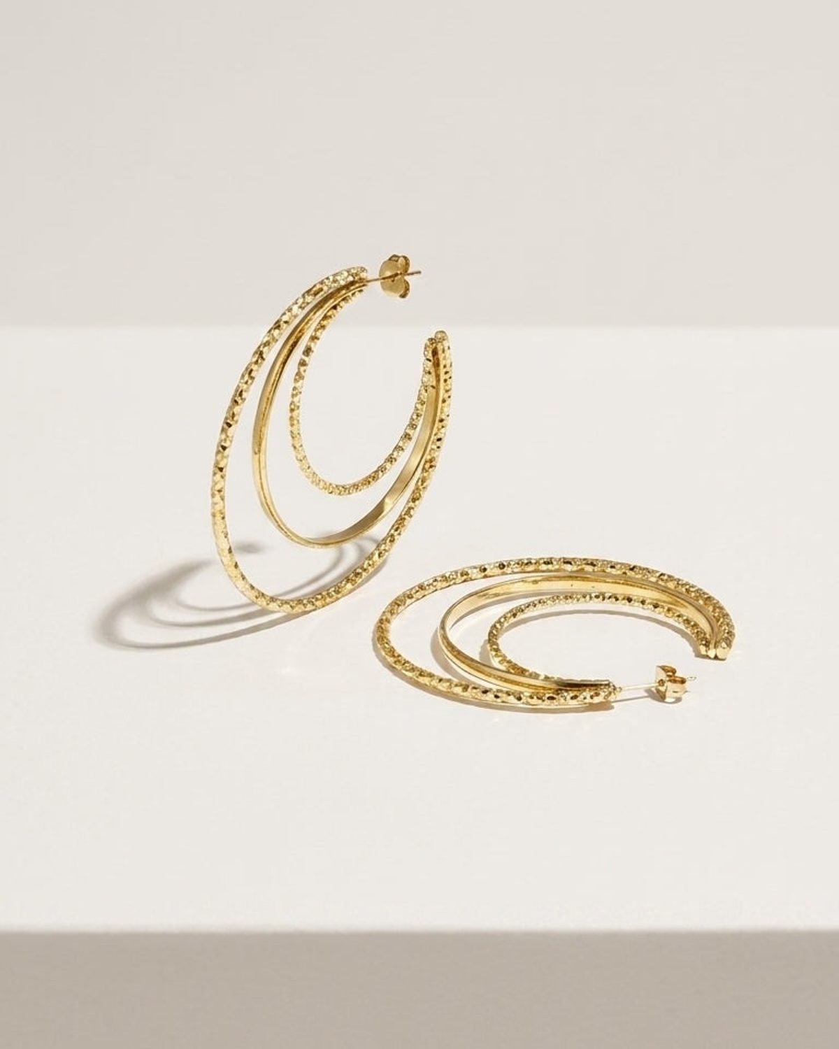 Stacked Aura Gold hoop earrings feature three concentric gold-plated loops with textured and smooth finishes.