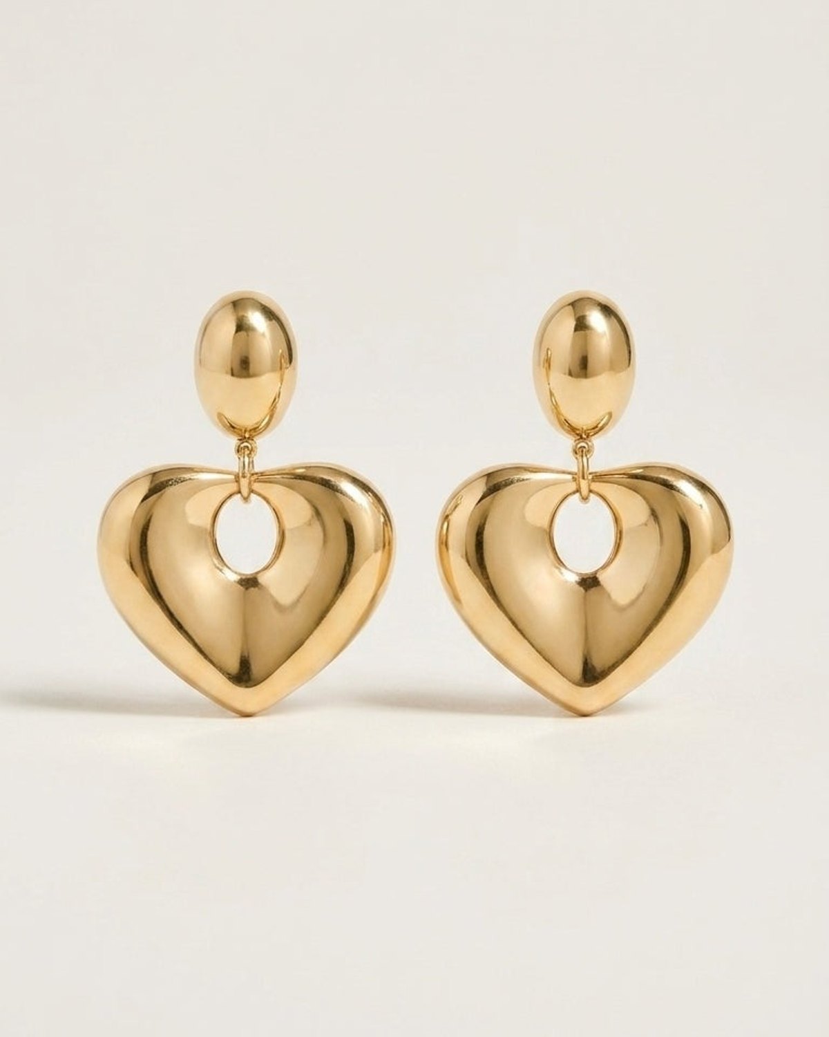 Polished gold-tone earrings featuring a smooth, puffed heart charm suspended from an oval stud.