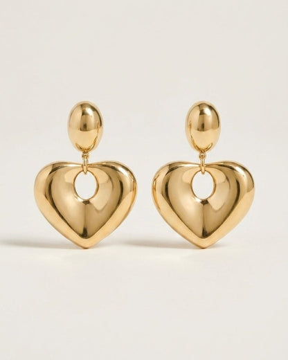 Polished gold-tone earrings featuring a smooth, puffed heart charm suspended from an oval stud.