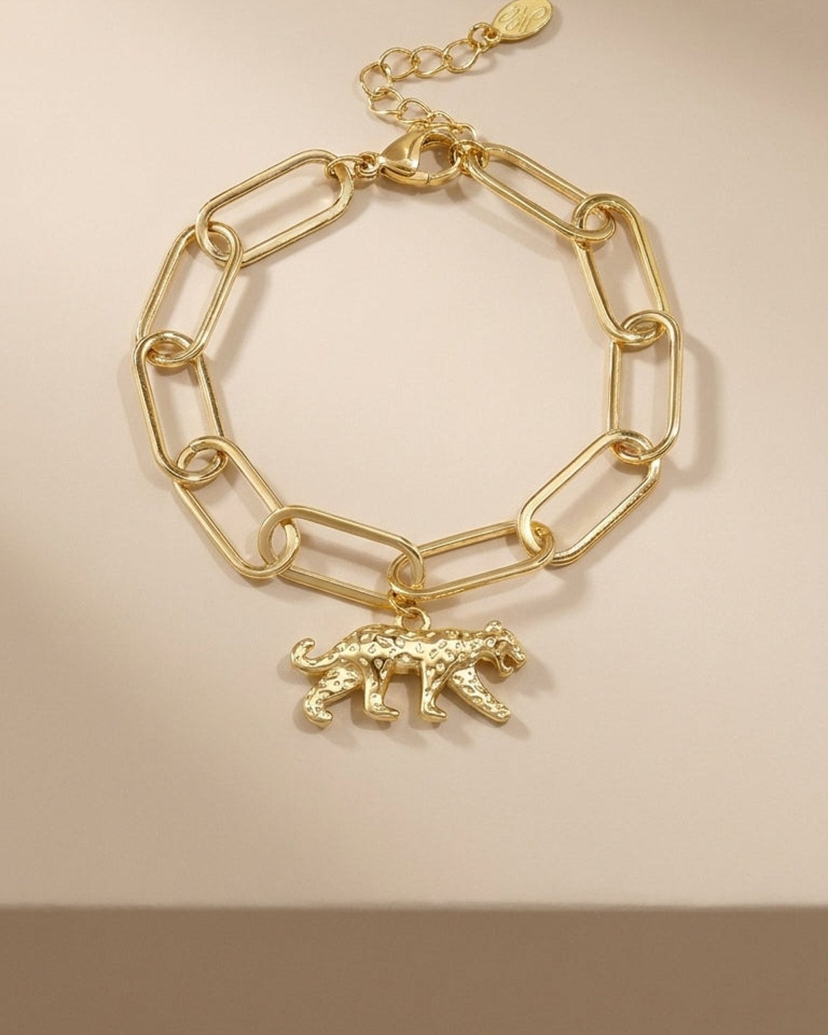 Gold link chain bracelet featuring a textured leopard charm with spots, on a beige background.