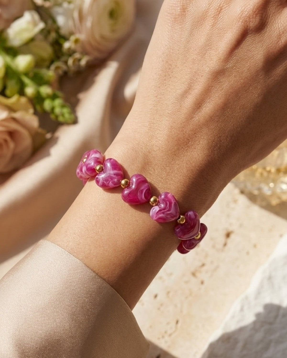 A bracelet of swirled pink resin heart beads separated by gold spheres, worn on a wrist.