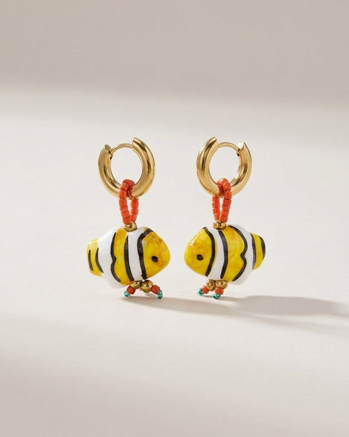 Glass fish bead earrings with gold hoops, orange seed beads, and yellow, white, and black striped fish pendants.