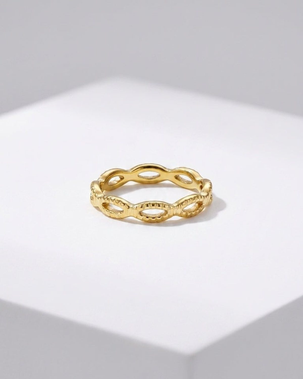 Gold band ring with an openwork braided or looped link design, centered on a white display surface.