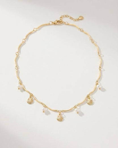 Gold necklace with a wavy chain, featuring dangling seashell charms and small white pearls.