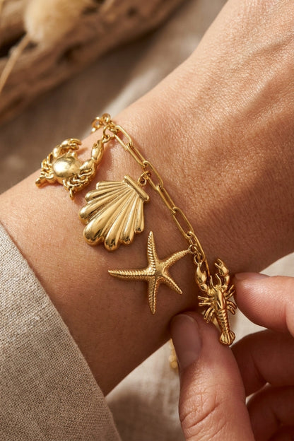 Gold bracelet with shell, starfish, and lobster charms on a wrist.