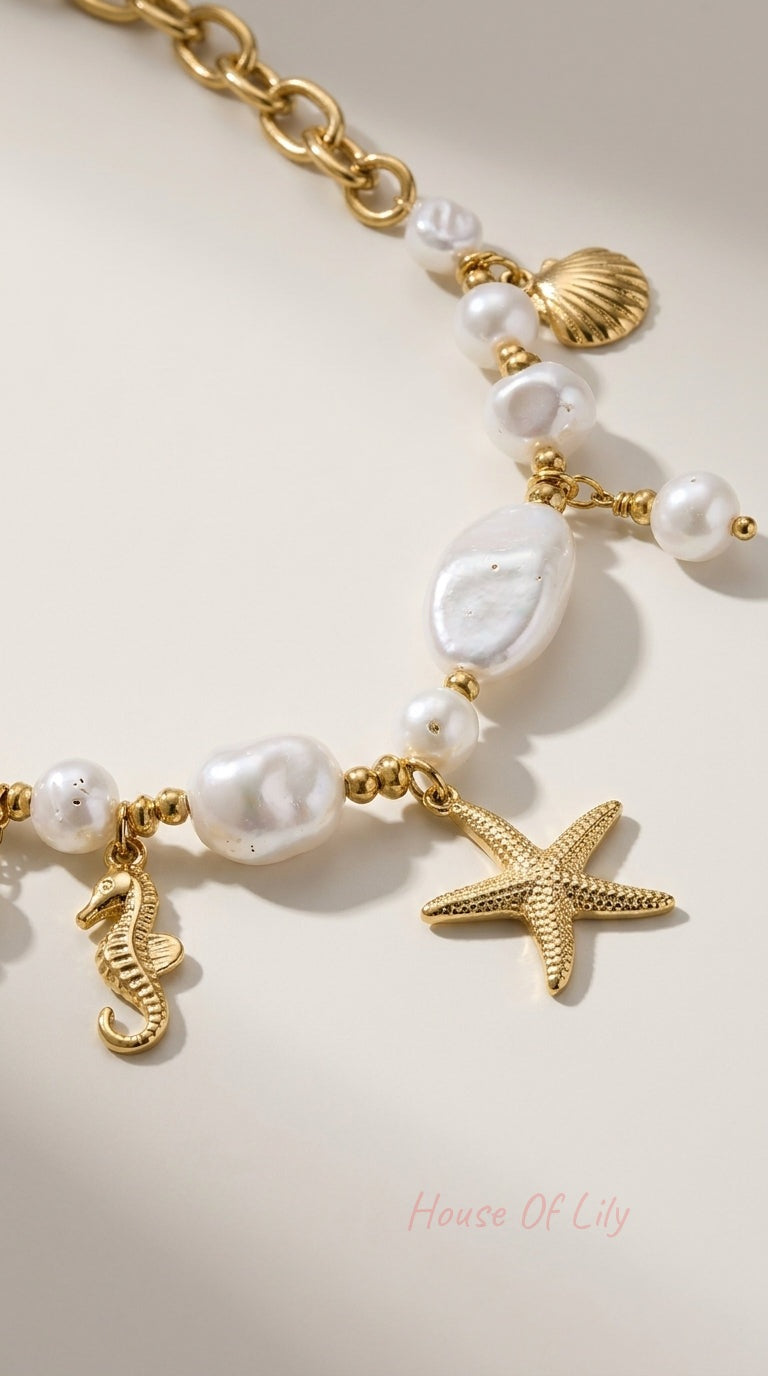 Gold chain bracelet featuring organic white pearls and ocean-themed charms: a starfish, seahorse, and seashell.