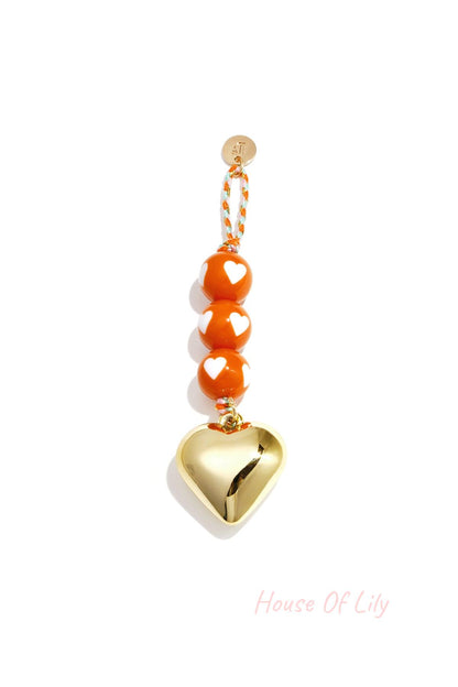 Orange heart charm bag keychain with gold heart pendant and heart-patterned beads on braided cord