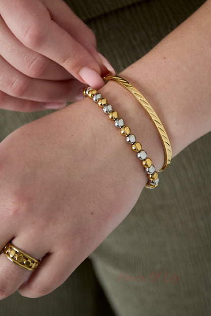 Close-up of a woman's wrist wearing the gold-tone twist metal bangle paired with a two-tone bead bracelet and gold ring