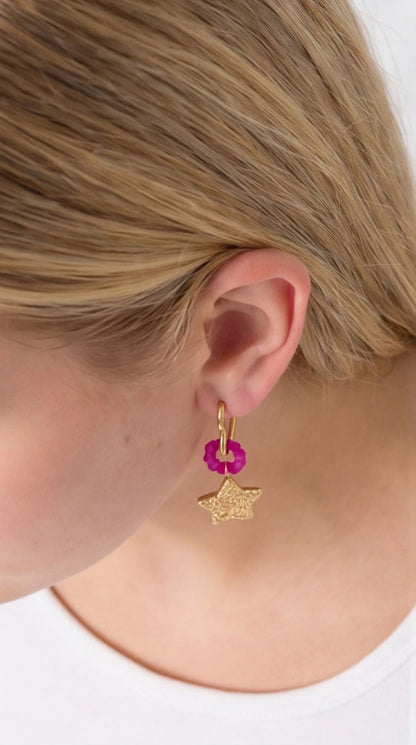 Shooting Star Drop earring featuring a textured gold star, a small pink flower accent, and a gold hoop on an ear.