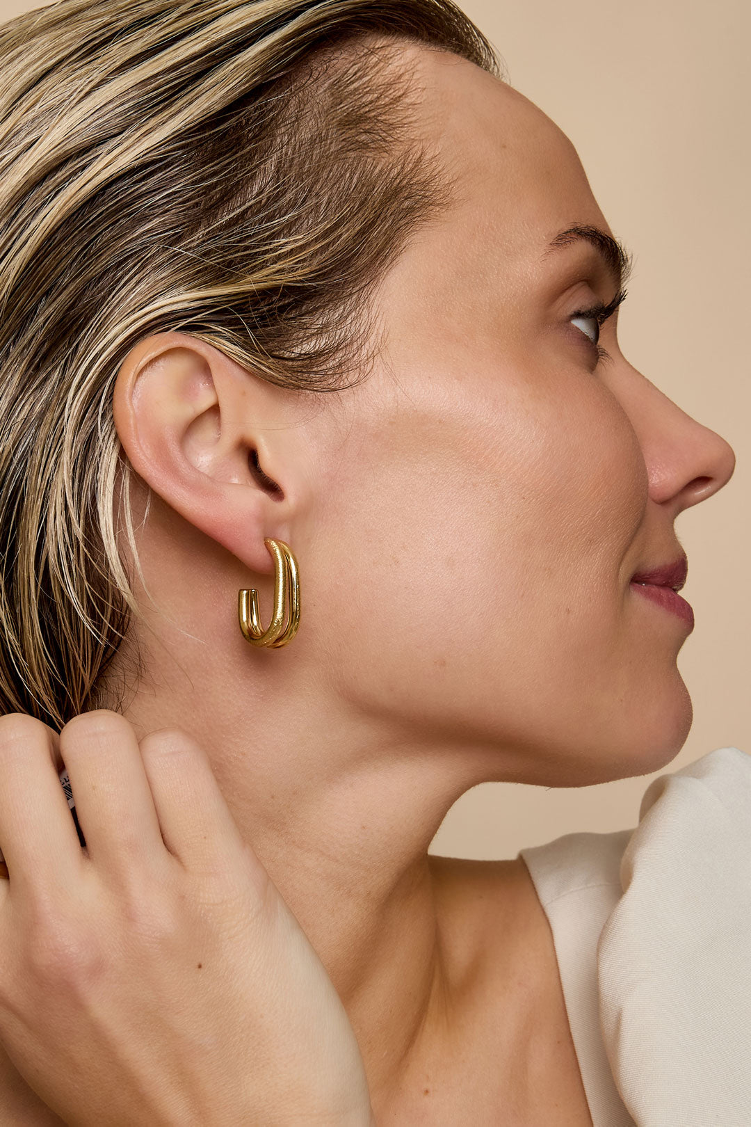 Profile view of woman wearing gold chunky double loop earrings showing youthful and minimalistic style