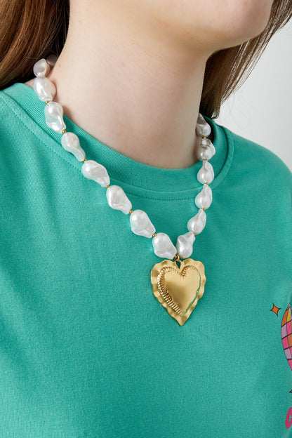 Woman wearing a playful baroque pearl necklace with a bold gold heart pendant over a green shirt