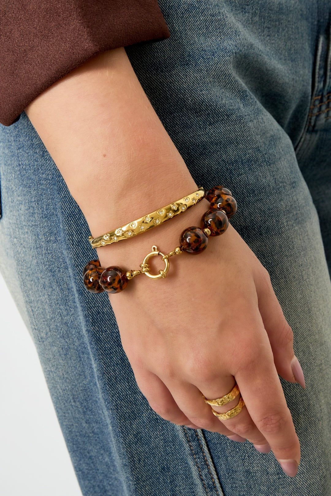 Woman wearing leopard print beaded bracelet with gold accents styled with blue jeans and gold rings on hand