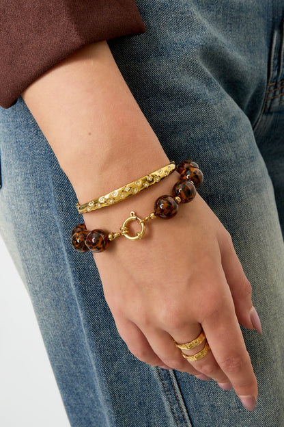 Woman wearing leopard print beaded bracelet with gold accents styled with blue jeans and gold rings on hand