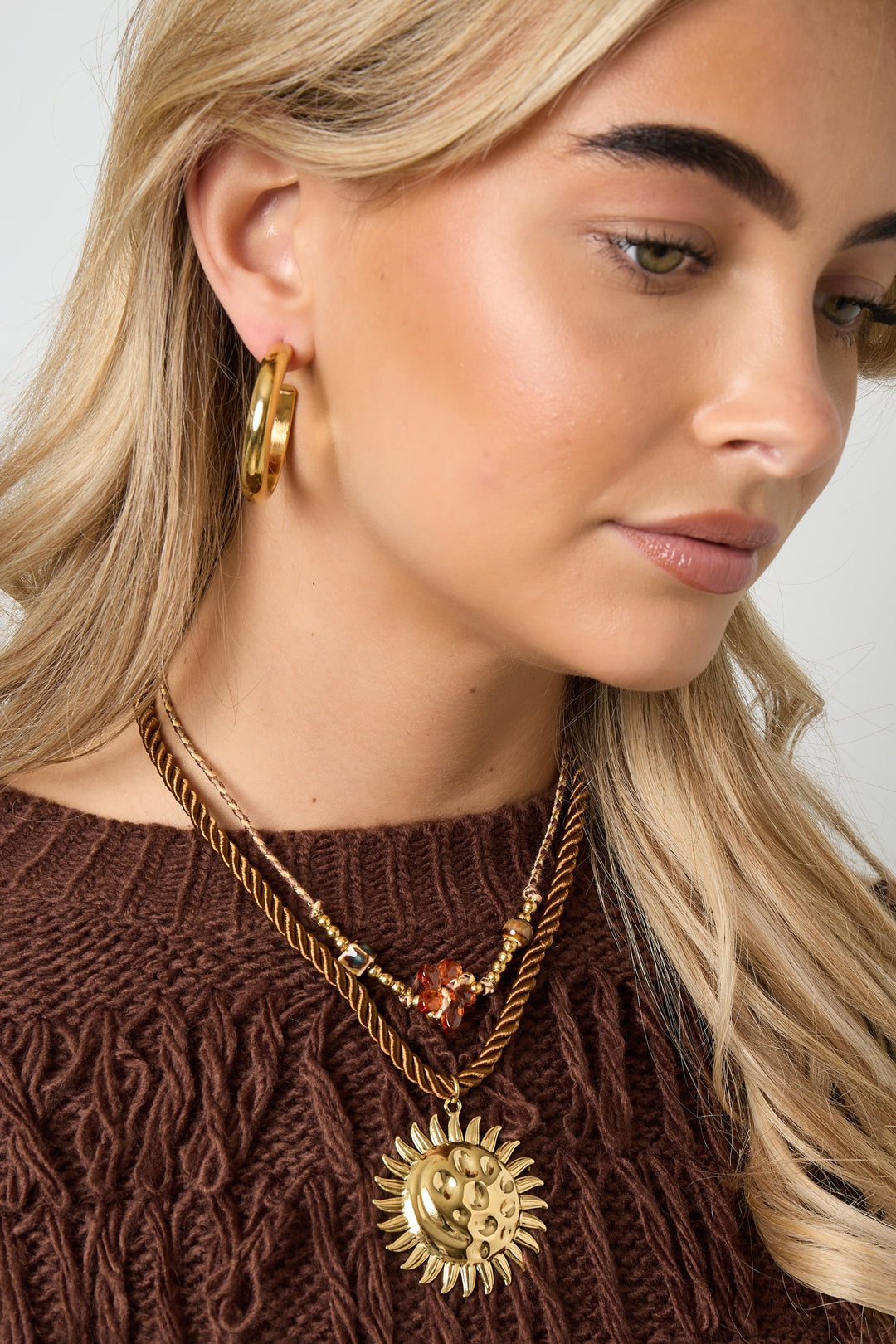 Side view of model wearing layered necklaces including flower beaded necklace and chunky gold hoop earrings