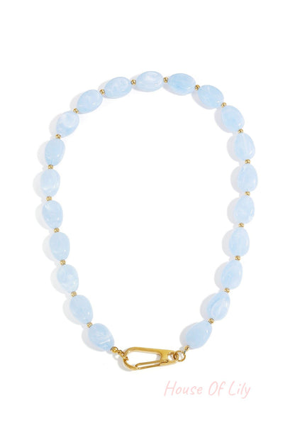 Baby blue acrylic beaded necklace with gold accents and clasp laid flat on white background