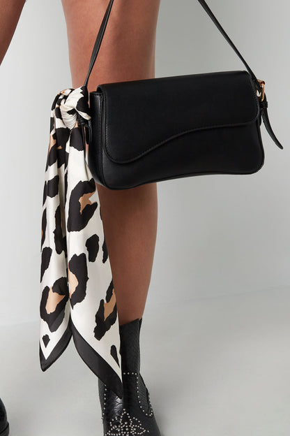 Woman carrying black handbag with beige and black leopard print scarf tied to strap, wearing black boots