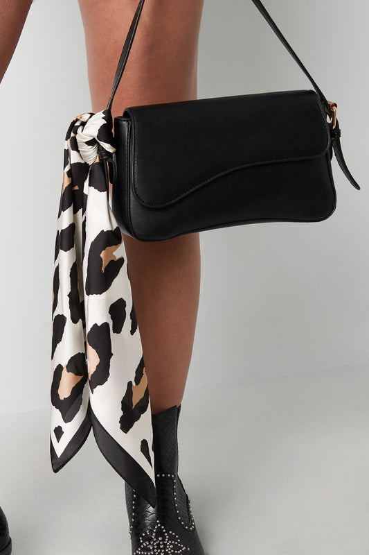 Woman carrying black handbag with beige and black leopard print scarf tied to strap, wearing black boots