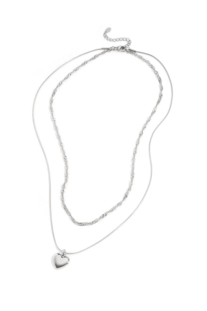 Silver two-layer necklace with twisted chain and heart-shaped pendant laid on white background