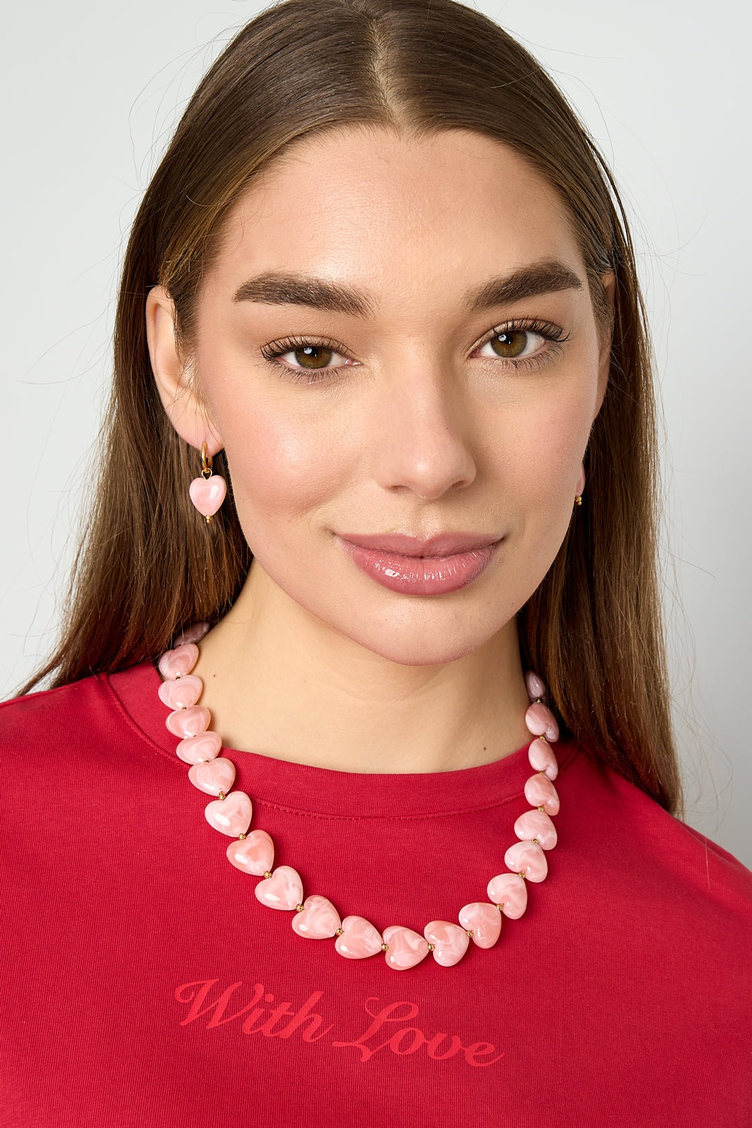 Model wearing pink heart-shaped bead necklace and matching earrings with red top