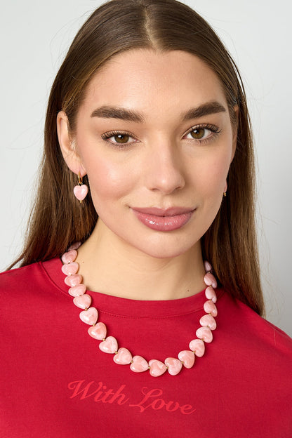 Model wearing pink heart-shaped bead necklace and matching earrings with red top