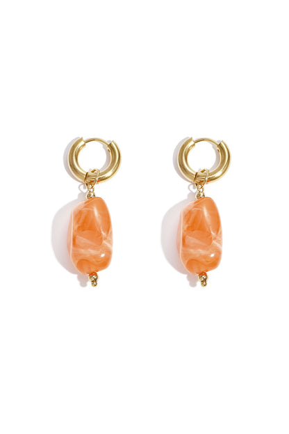 Gold hoop earrings with irregular berry red resin drop beads on white background