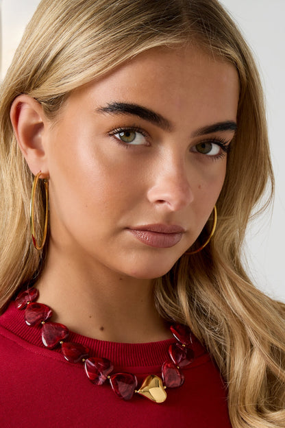Model portrait showing the red heart bead necklace, hoop earrings, and a red sweater, emphasizing youthful and boutique style
