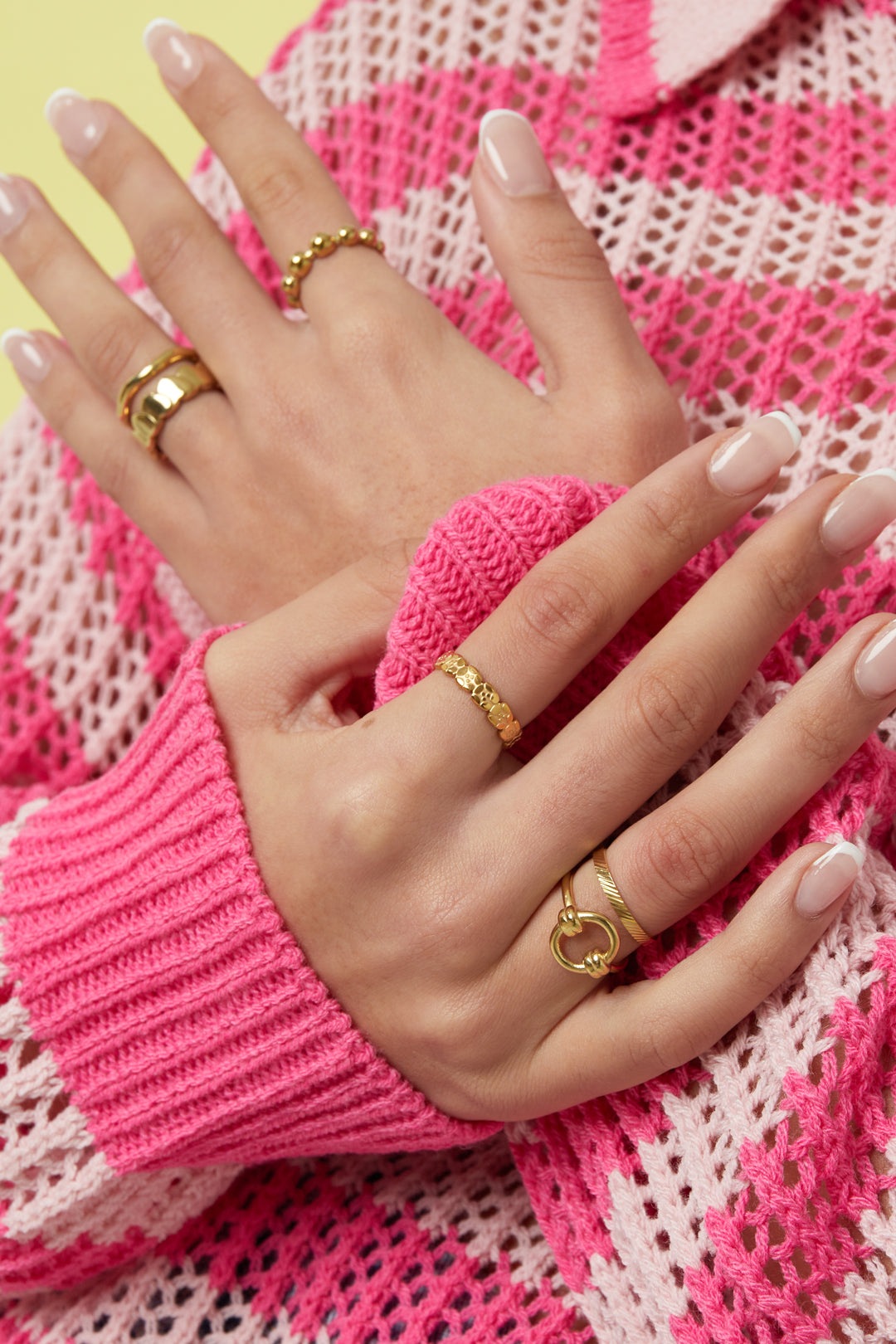 Woman wearing multiple stylish gold rings including a minimalist textured band paired with pink knitwear
