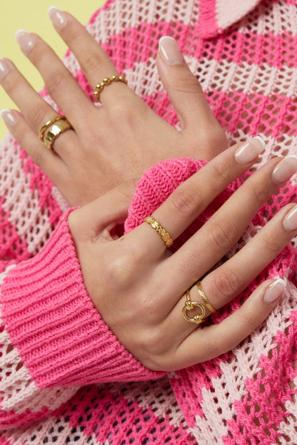 Woman wearing multiple stylish gold rings including a minimalist textured band paired with pink knitwear