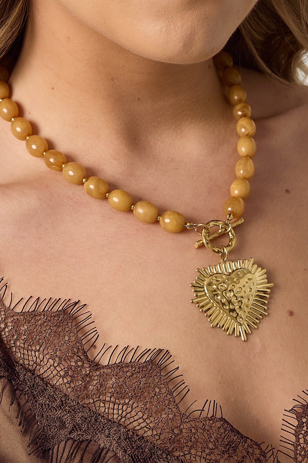 studio shot of nude beige beaded necklace with gold textured heart pendant and toggle clasp