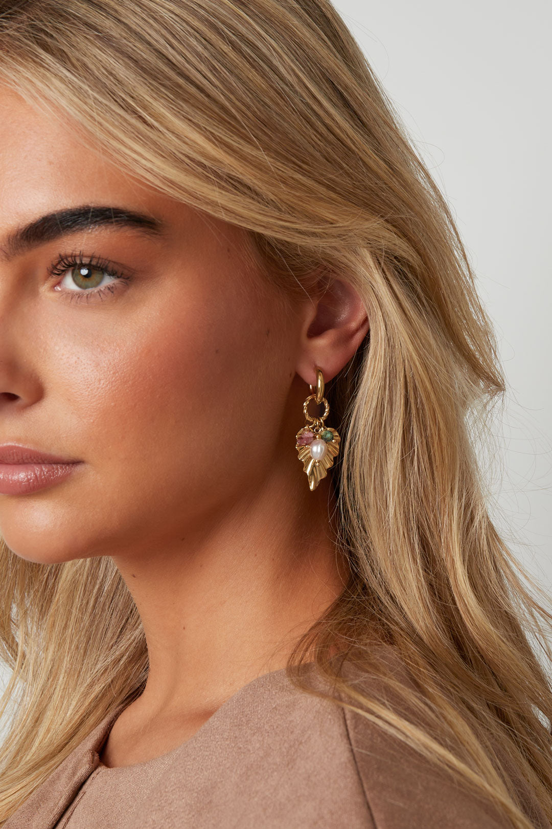 Close-up of a woman wearing gold-tone leaf drop earrings featuring a decorative pearl and colorful stones