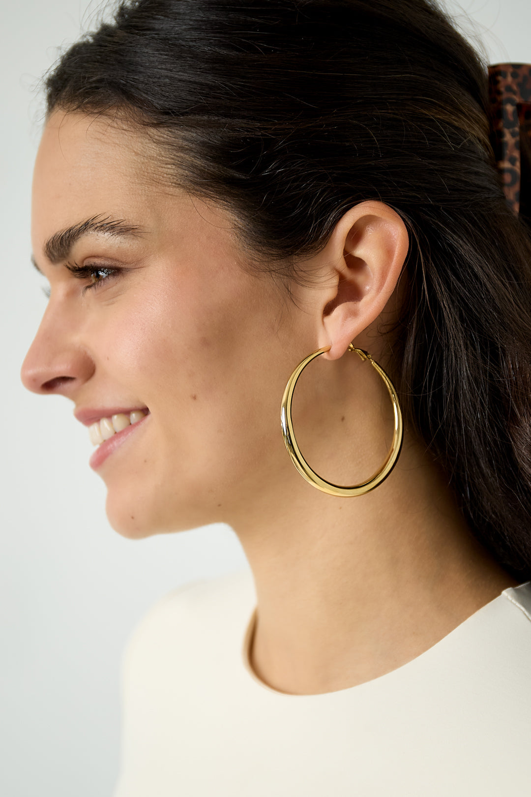 Close-up profile of woman wearing polished gold hoop earring with dark hair pulled back