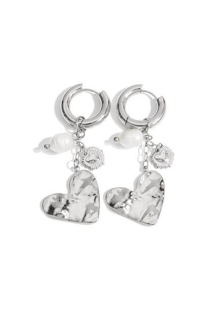 Silver hoop earrings with hammered heart charms, pearl accents, and small heart dangles on white background