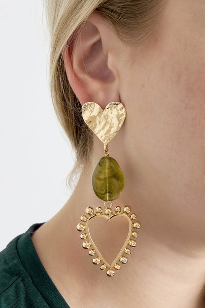 Close-up of a woman wearing heart drop earrings featuring hammered gold heart studs, olive green marbled resin bead, and gold beaded open heart frame