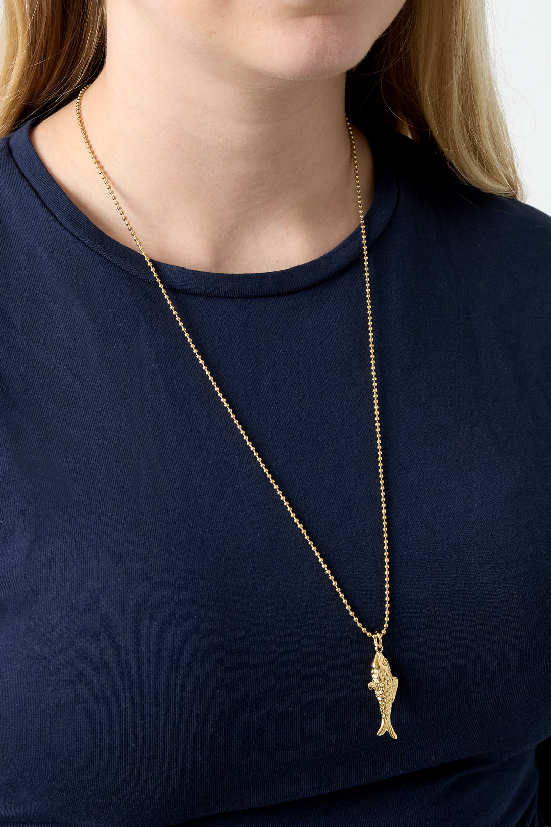 Model wearing gold fish pendant necklace with navy blue shirt