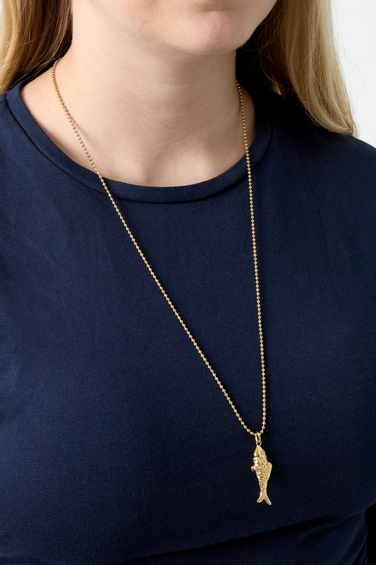 Model wearing gold fish pendant necklace with navy blue shirt