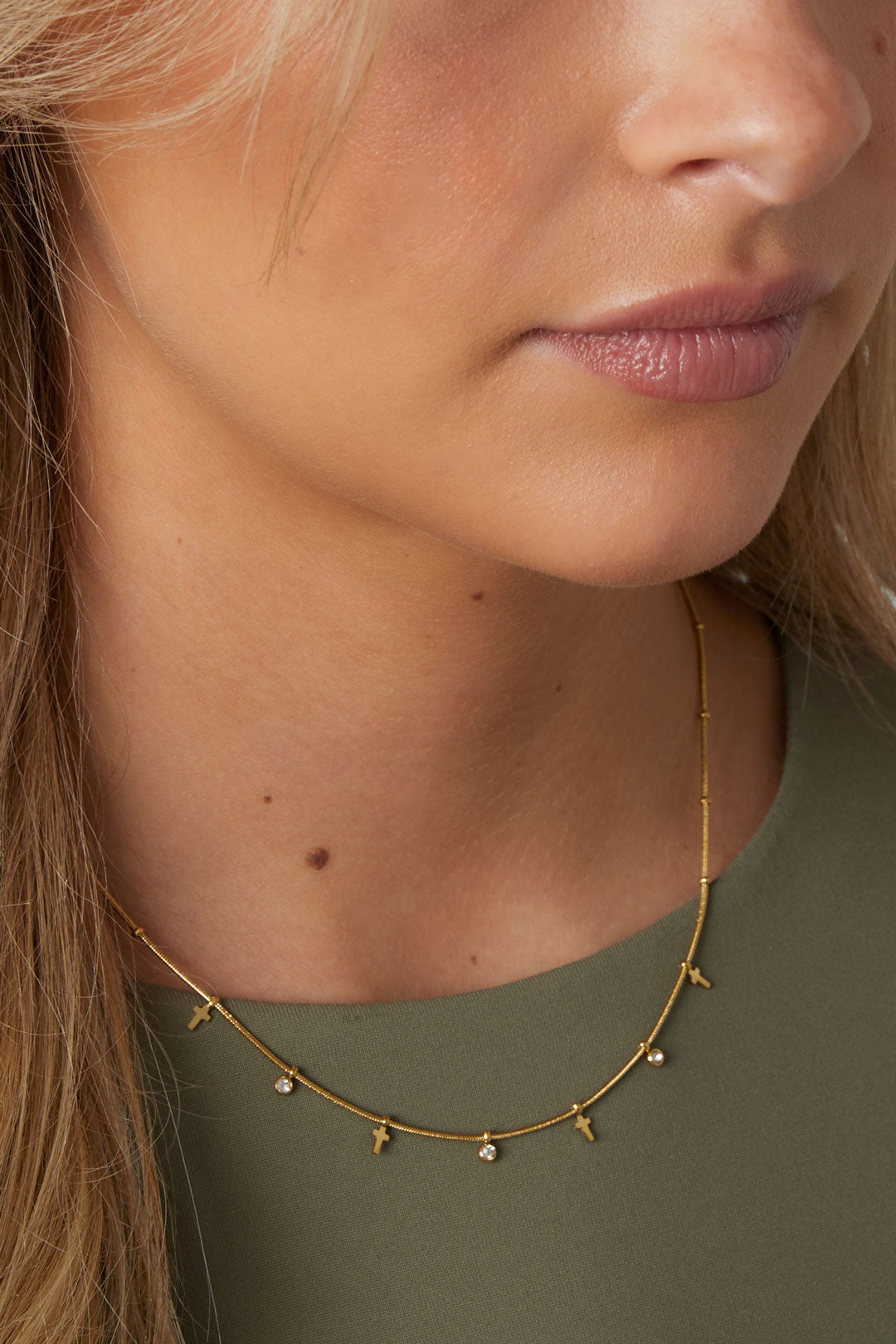 Close-up of woman wearing the delicate gold cross necklace with rhinestones