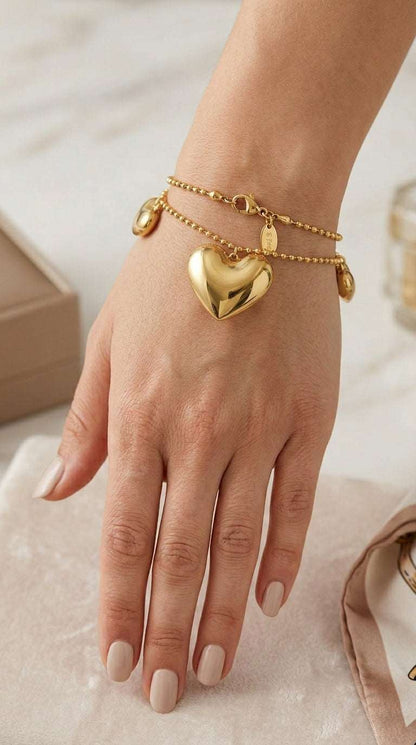 Gold double-strand beaded bracelet featuring a large, polished puffy heart charm and small heart accents.
