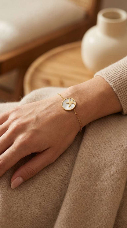 Gold chain bracelet featuring a round, iridescent mother-of-pearl charm with a cutout starfish design.