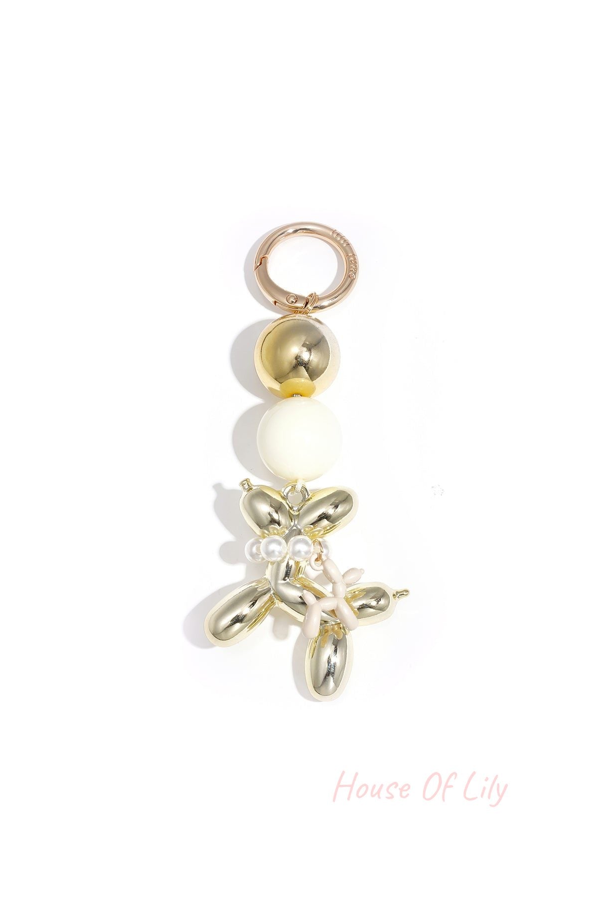 Gold-tone balloon dog keychain with white acrylic bead and pale pink balloon charm on white background